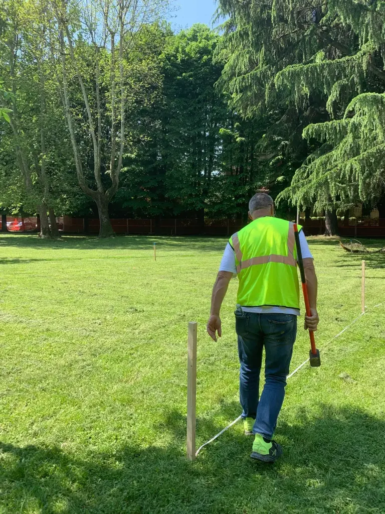 Ein Techniker in Warnweste steckt vor Baubeginn eine Wiese ab